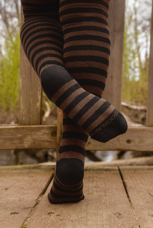 A person wearing black and dark brown fairy striped thigh-high socks, on a wooden deck.