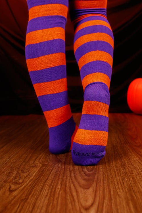 Person wearing striped orange and purple thigh high's against a dark background.