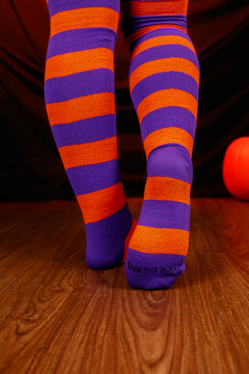 Person wearing striped orange and purple thigh high's against a dark background.