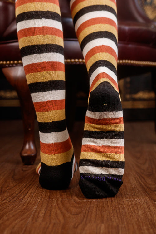 Striped socks with orange, black, and white pattern on a wooden floor.