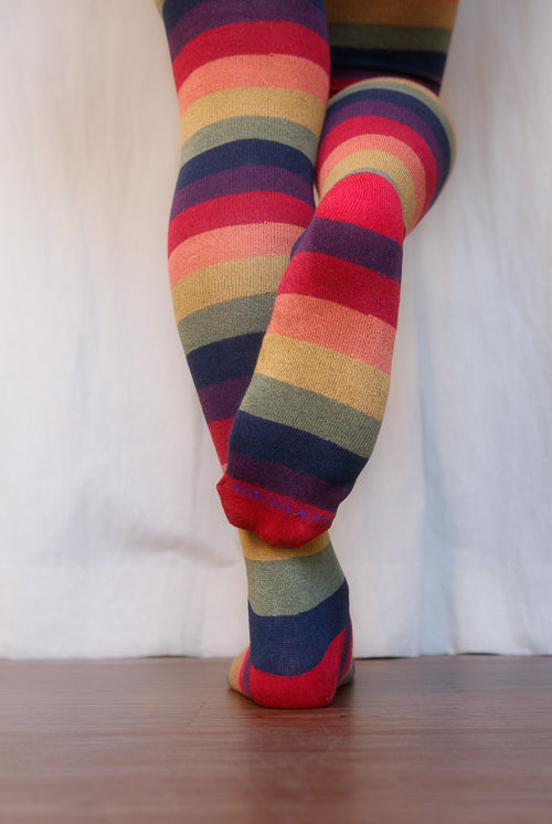 A person wearing XL foot longer harvest rainbow thigh highs in rainbow stripes