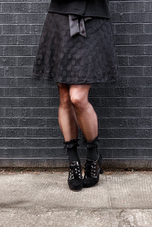 A person wearing lace ruffle anklets with mini bows in black on black