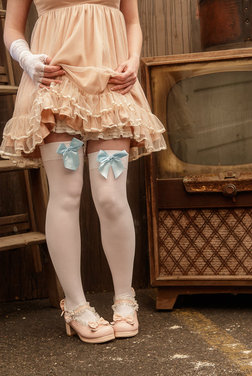 A person wearing opaque thigh high stockings in white with a light blue bow