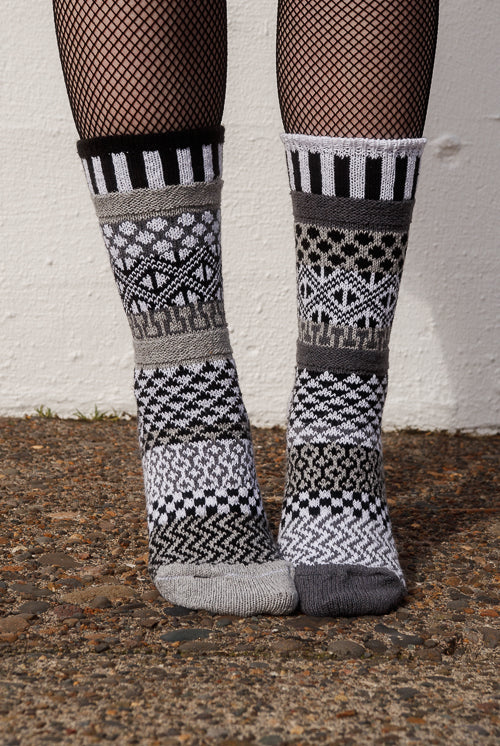 Person wearing fishnet stockings and patterned socks against a white wall.