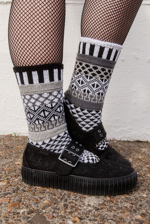 Person wearing fishnet stockings and patterned socks against a white wall.