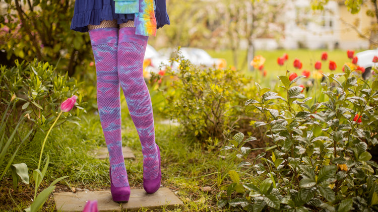model wearing tie dyed socks and holding two other pair standing in a garden full of tulips