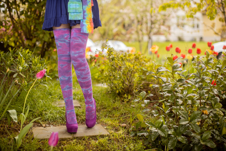 model wearing tie dyed socks and holding two other pair standing in a garden full of tulips