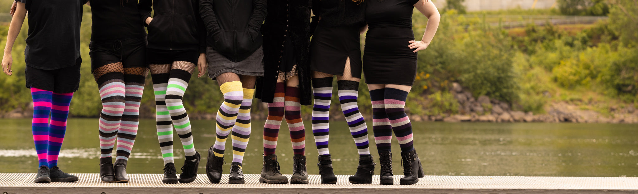 Seven people, each one wearing a pair of thigh high socks patterned after a different LGBTQIA+ pride flag. They stand in a row with arms around each other's shoulders.