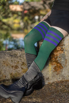 Person wearing green knee-high socks with purple stripes, sitting on a stone wall outdoors.