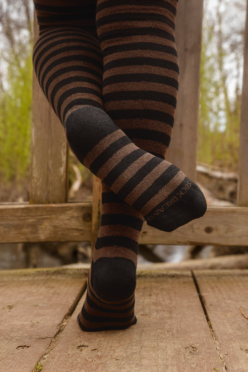 A person wearing black and dark brown fairy striped thigh-high socks, on a wooden deck.