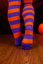 Person wearing striped orange and purple thigh high's against a dark background.