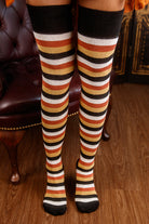 Striped knee-high socks with black, orange, and white pattern worn indoors.