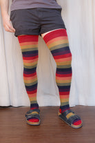 A person wearing XL foot longer harvest rainbow thigh highs in rainbow stripes