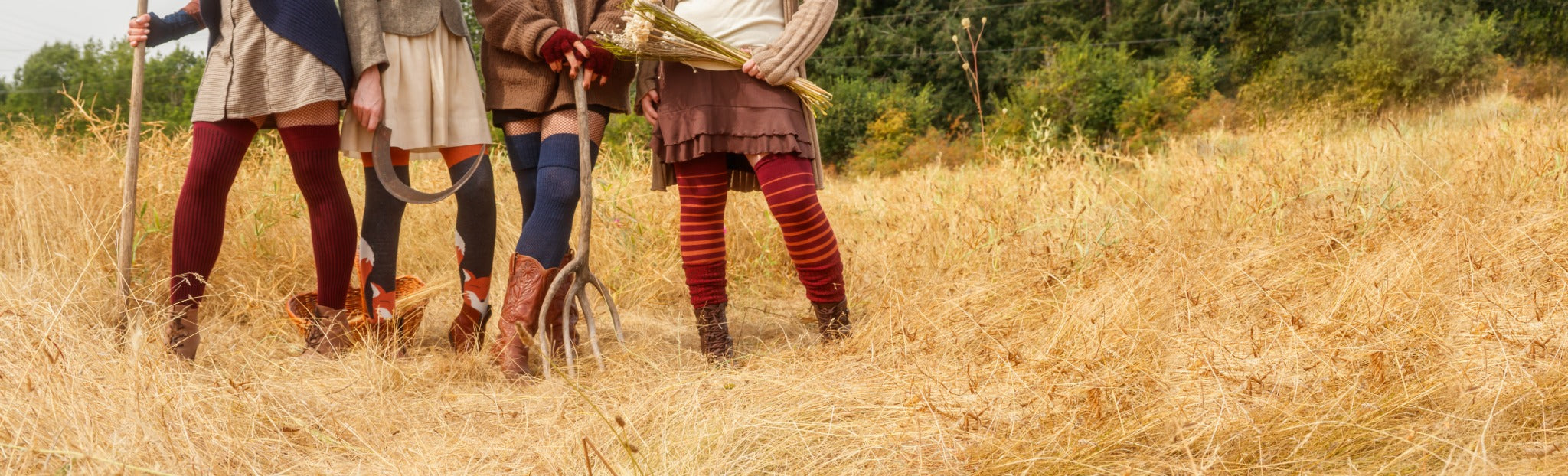 A group of models wearing autumnal socks with earth toned outfits stands in a field with harvest tools