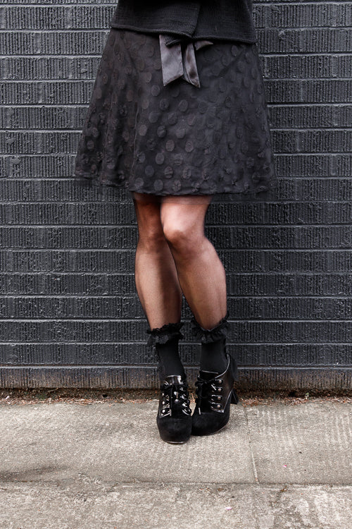 A person wearing lace ruffle anklets with mini bows in black on black