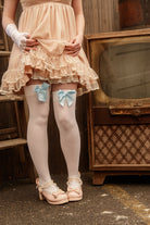 A person wearing opaque thigh high stockings in white with a light blue bow