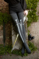 Person wearing dark charcoal thigh highs with a sword design down the front