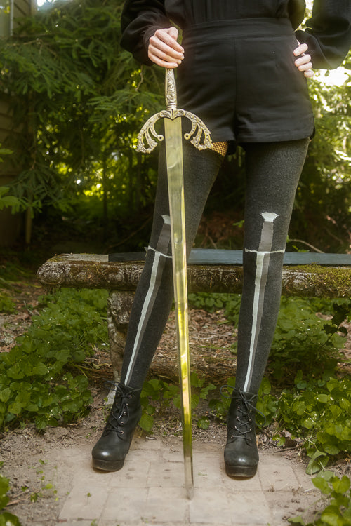 Person wearing dark charcoal thigh highs with a sword design down the front