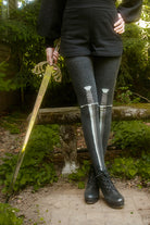 Person wearing dark charcoal thigh highs with a sword design down the front