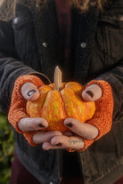 A person wearing chenille fingerless gloves in pumpkin holding a pumpkin