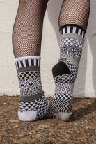 Person wearing fishnet stockings and patterned socks against a white wall.