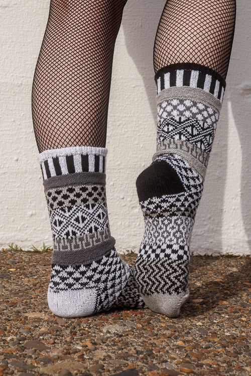 Person wearing fishnet stockings and patterned socks against a white wall.