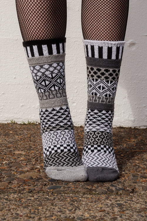Person wearing fishnet stockings and patterned socks against a white wall.
