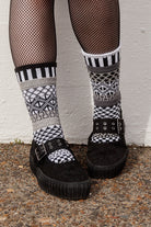 Person wearing fishnet stockings and patterned socks against a white wall.