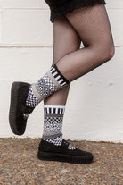 Person wearing fishnet stockings and patterned socks against a white wall.