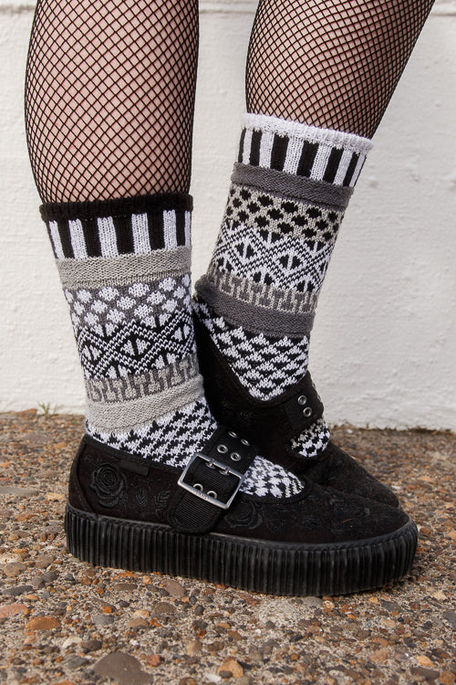 Person wearing fishnet stockings and patterned socks against a white wall.