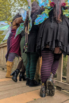 A group of four people wearing different colors of Faery stripes and fairy wings, standing on a wooden bridge.