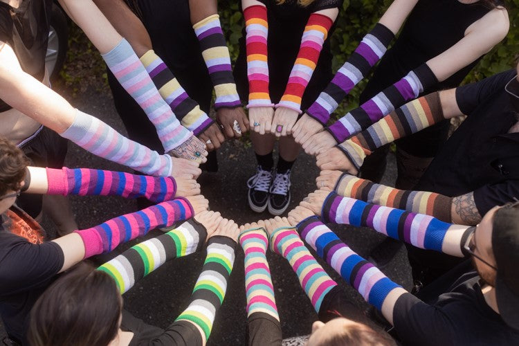 A group of models wearing Pride Flag striped sleeves, standing in a circle with their hands together in the center